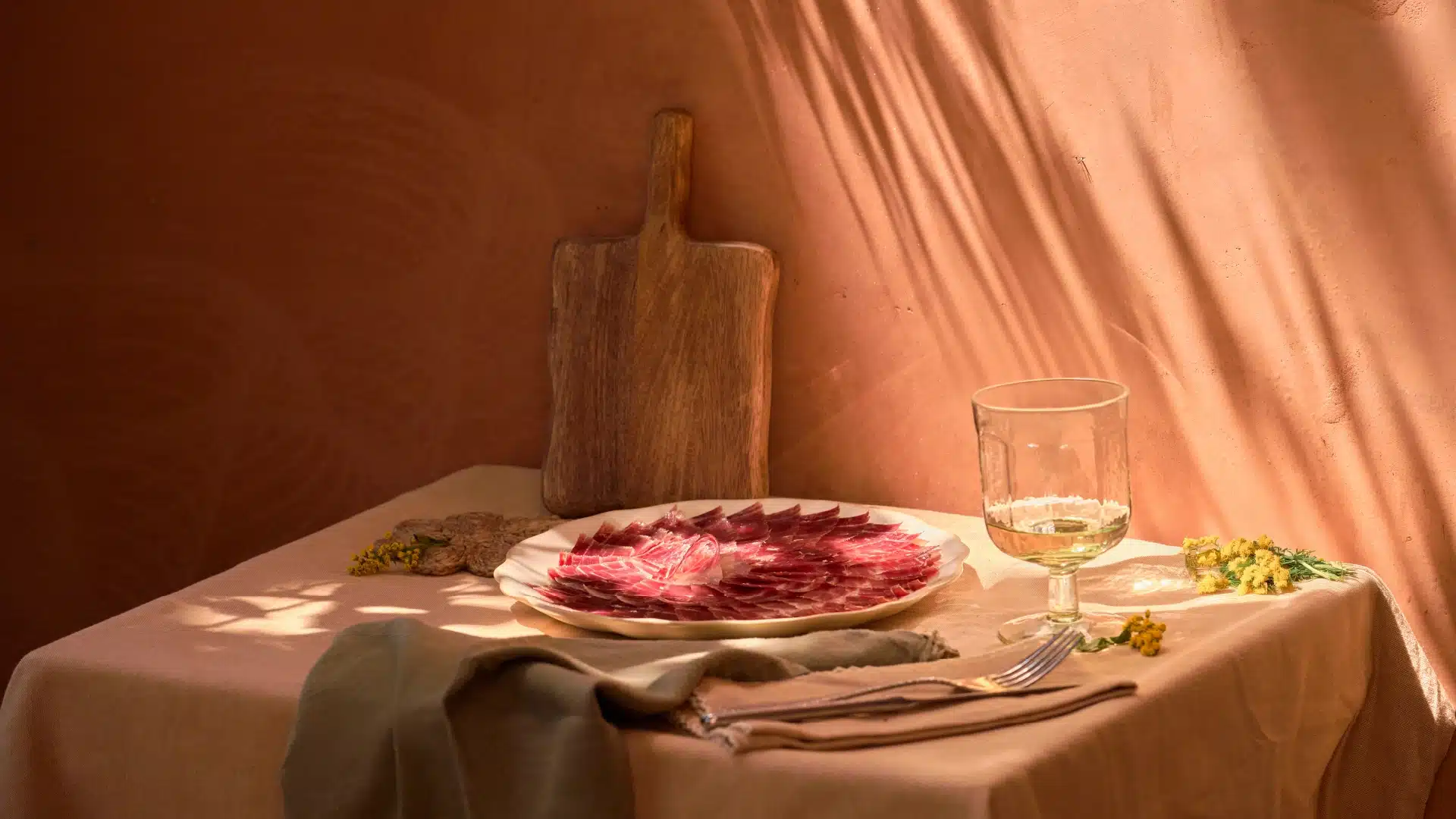 Bodegón gourmet de jamón ibérico recién cortado, tabla de madera y copa sobre mesa